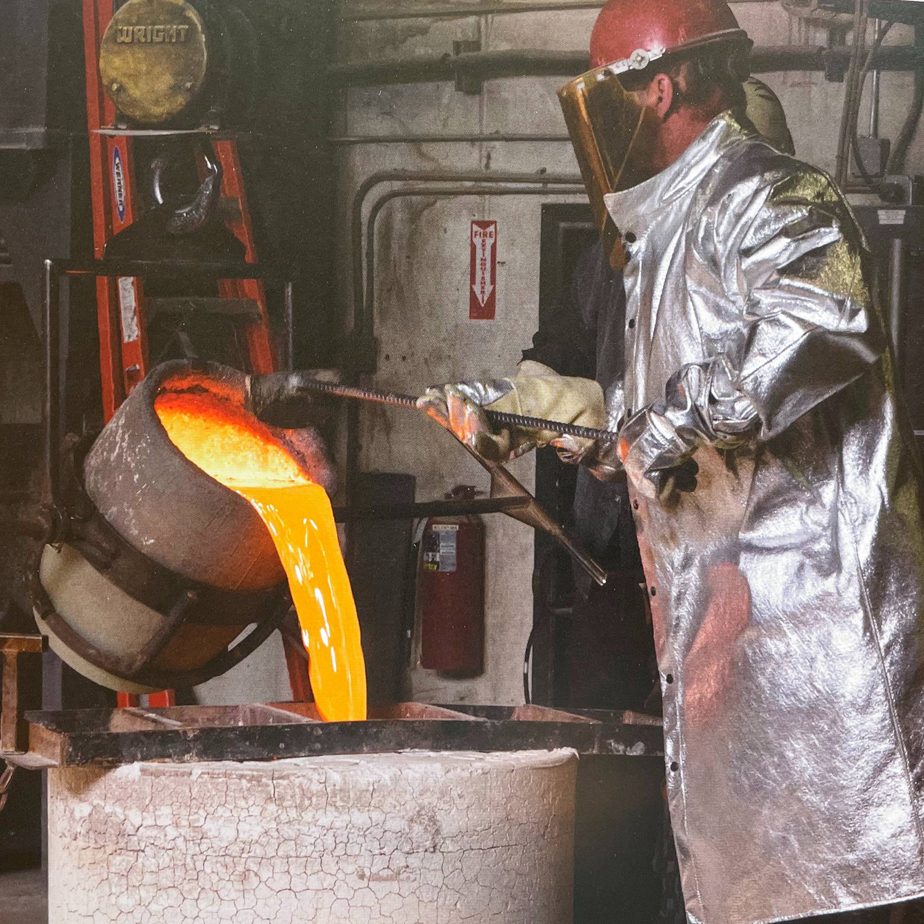 person in protective gear pour molten bronze into a mold